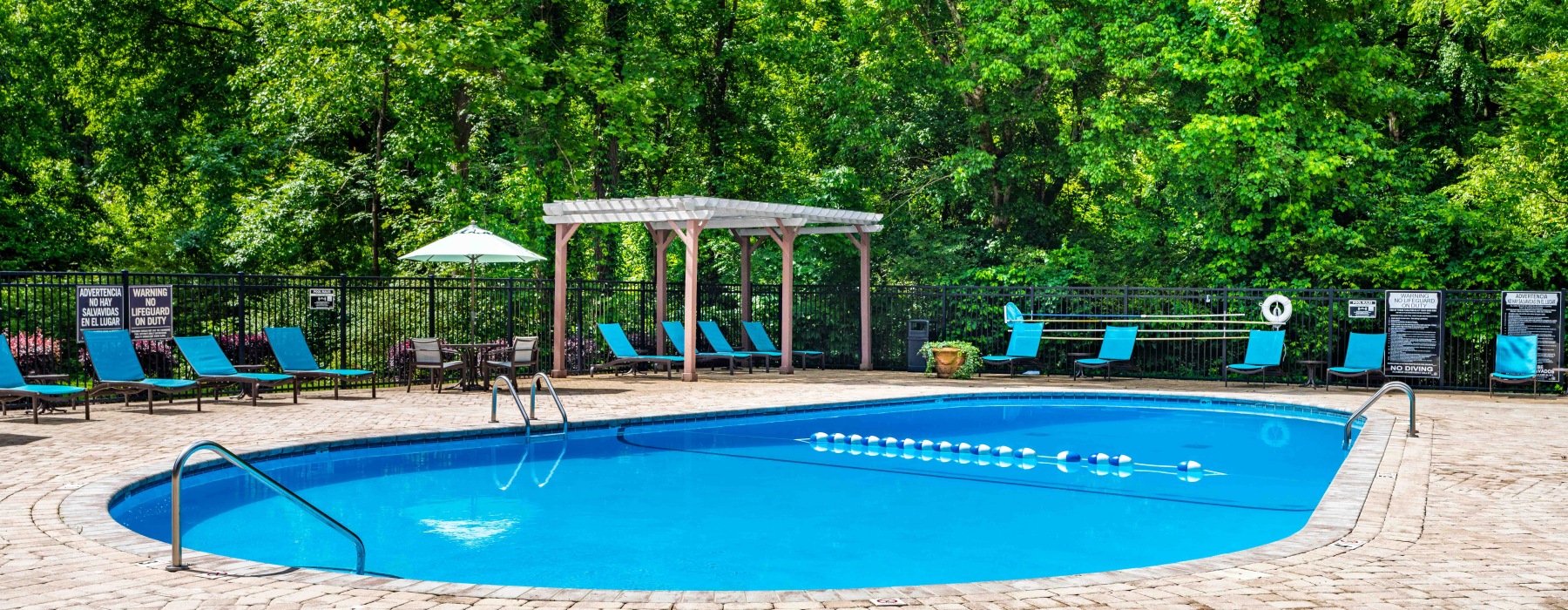 fenced in pool area with umbrella shaded tables and chairs