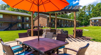 Social area with pergola covered grills and umbrella shaded table and chairs 