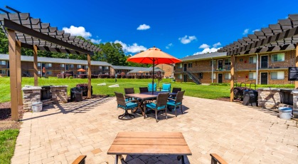Social area with pergola covered grills and umbrella shaded table and chairs 