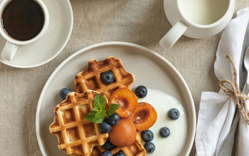 a plate of blueberries and waffles and a cup of coffee