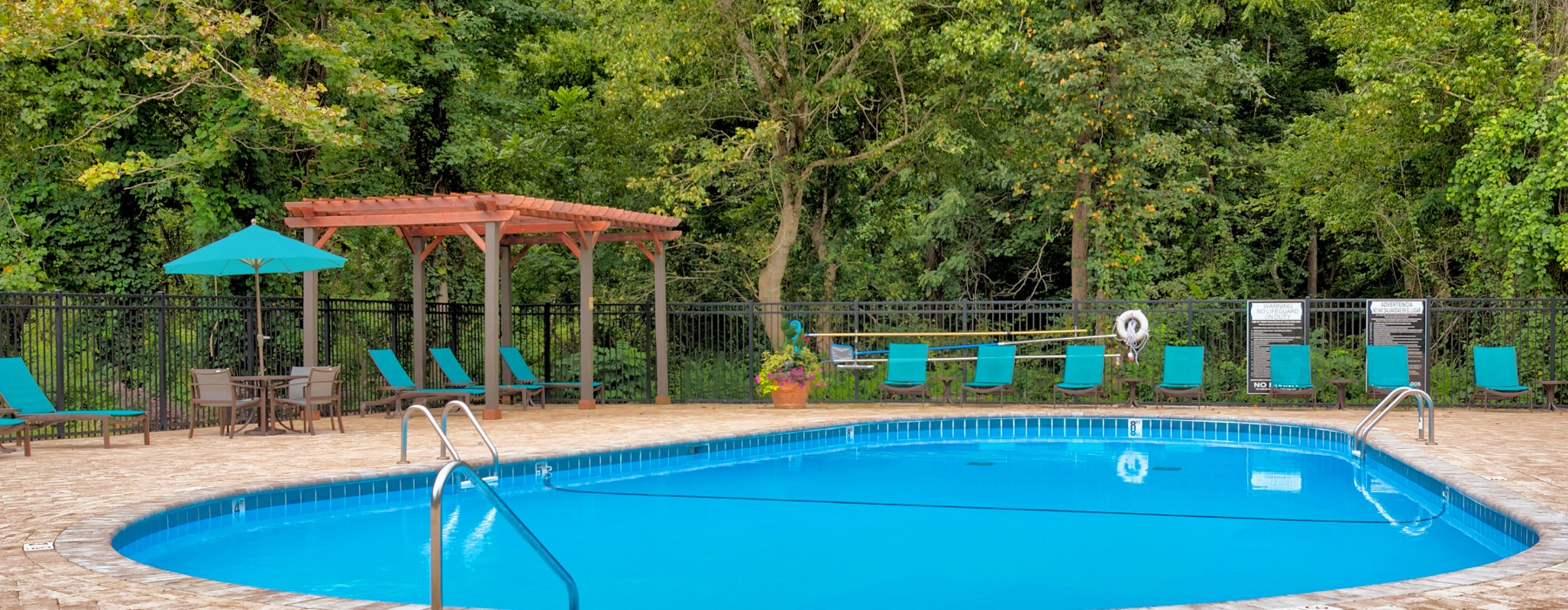 fenced in pool area with umbrella shaded tables and chairs