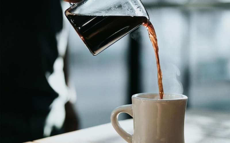 a person pouring a carafe of coffee into a cup