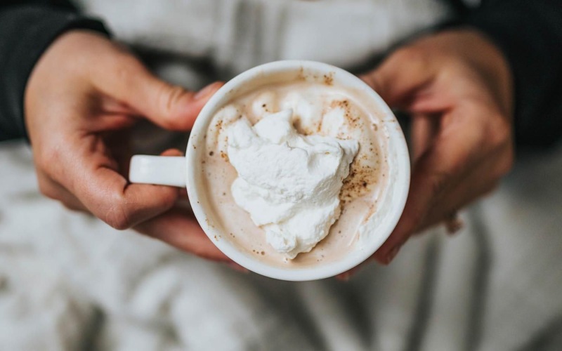 a person, in bed, holding a cup of coffee