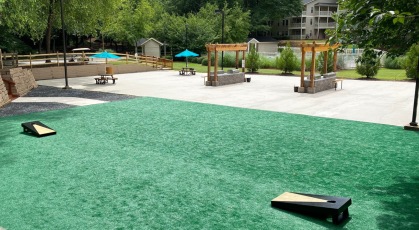 Large social patio with artificial grass, corn hole game, pergolas, and lounge furniture