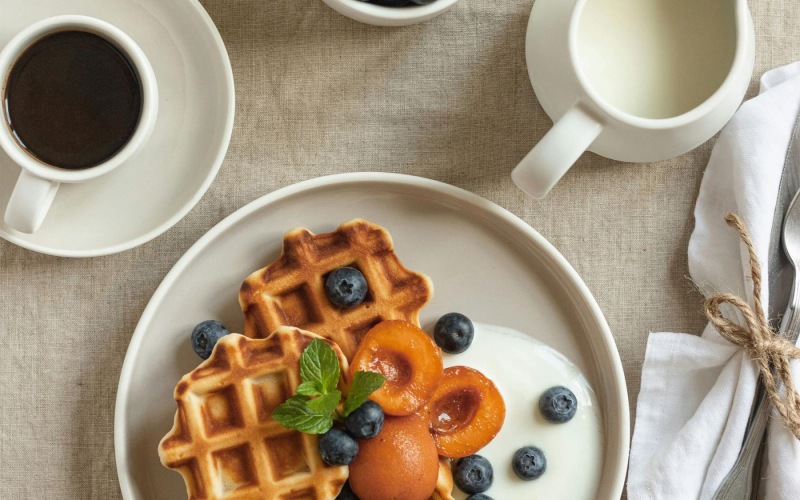 a plate of blueberries and waffles and a cup of coffee