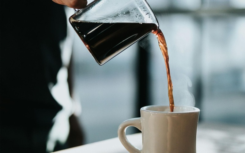 a person pouring a carafe of coffee into a cup