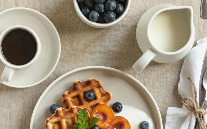 a plate of blueberries and waffles and a cup of coffee