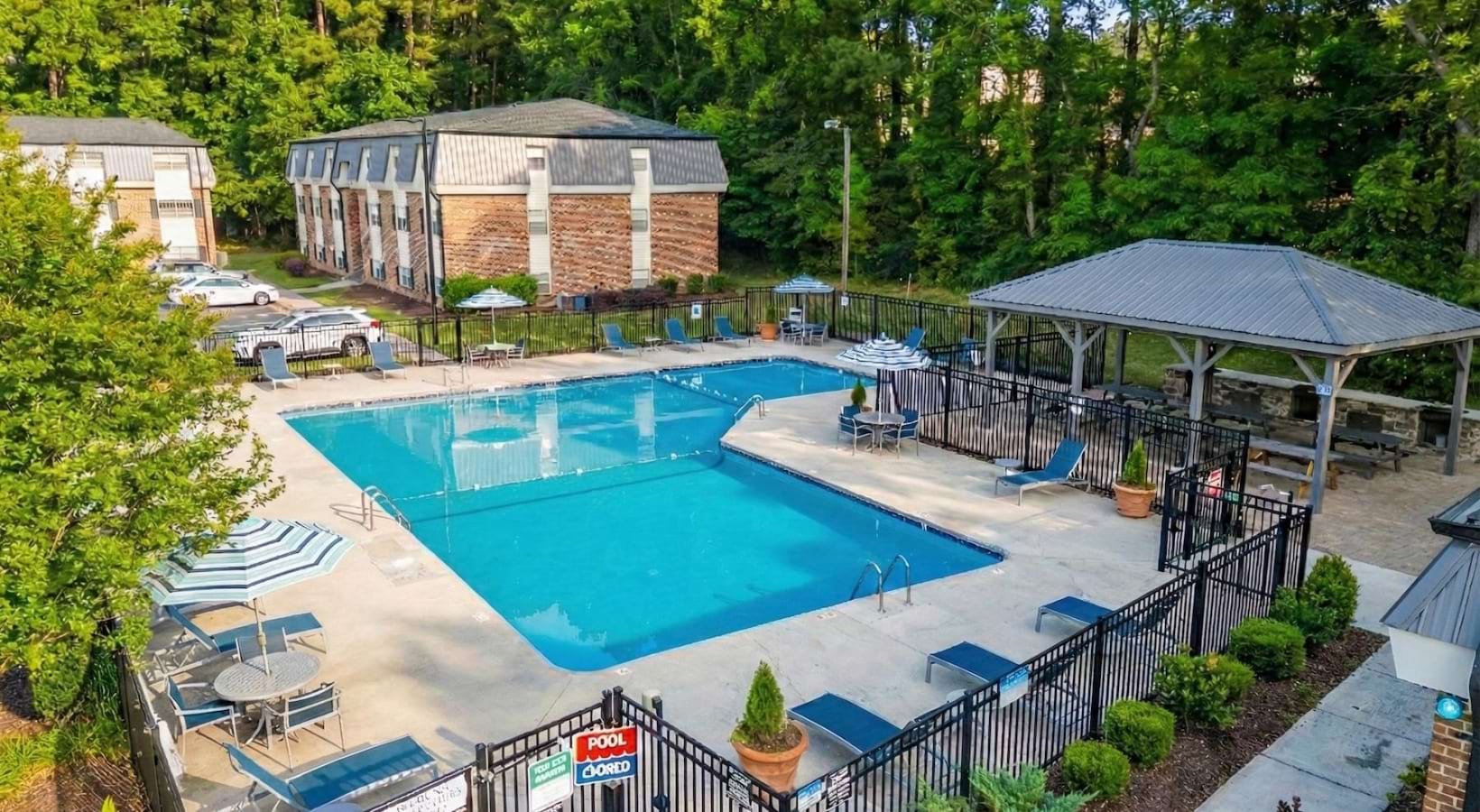 Sparkling blue pool surround by large trees and lounge chairs