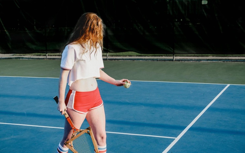 woman walks across a tennis court holding a racket and ball