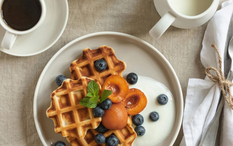 a plate of blueberries and waffles and a cup of coffee