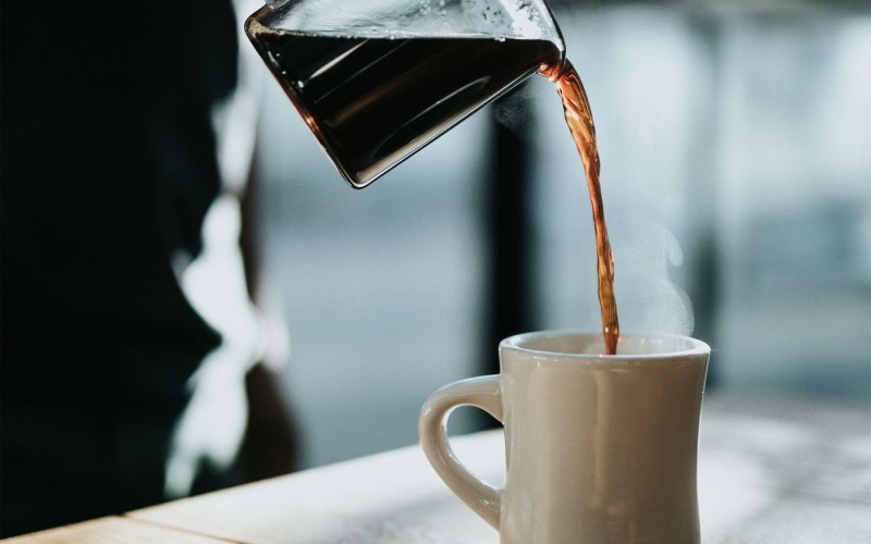 a person pouring a carafe of coffee into a cup