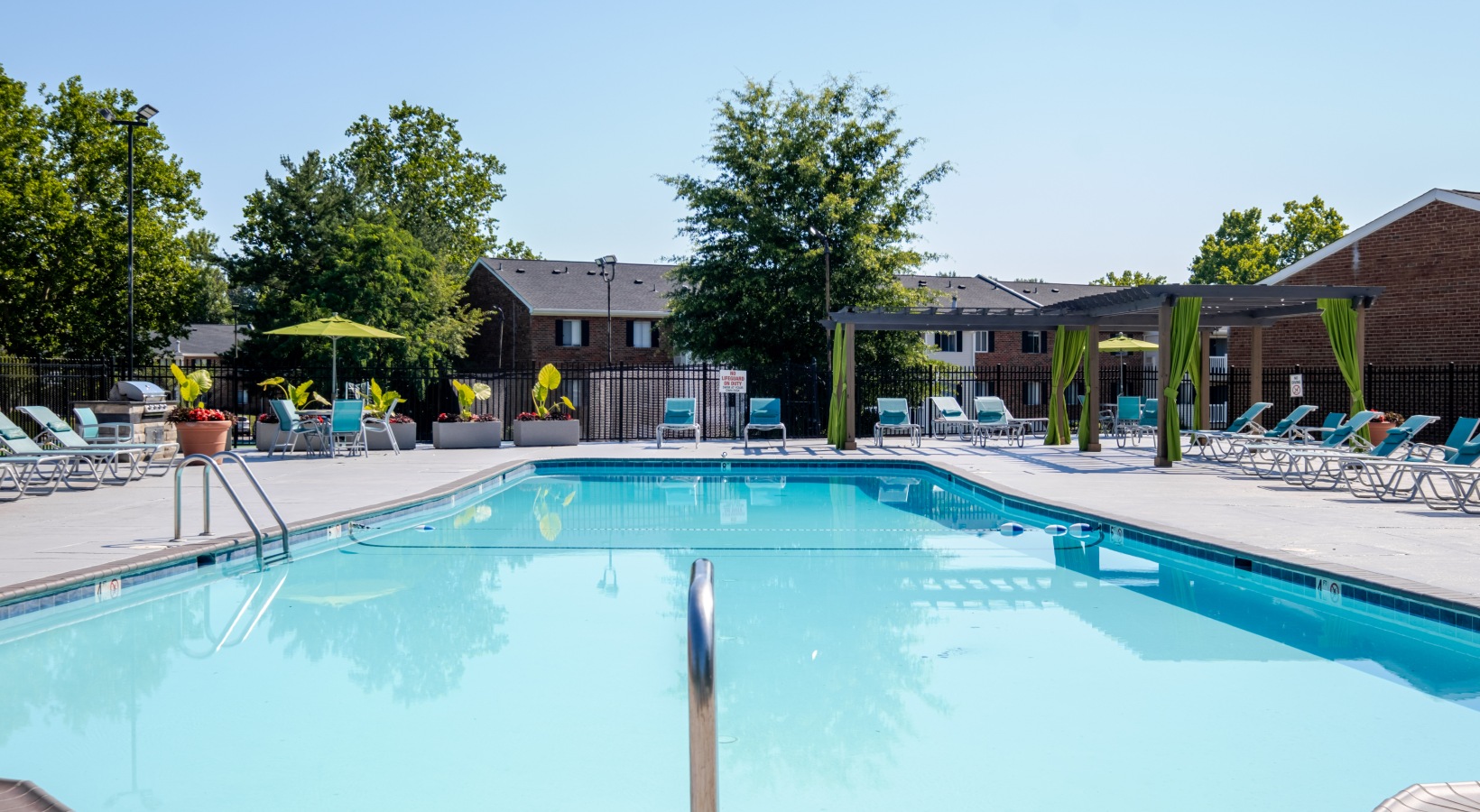 Sparkling blue pool surround by large trees and lounge chairs