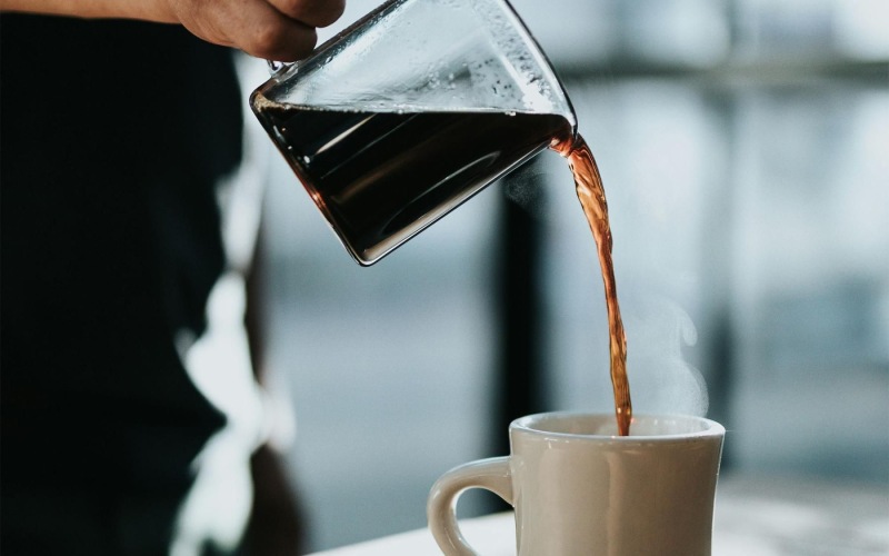 a person pouring a carafe of coffee into a cup