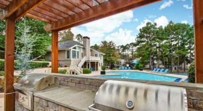 Gas grill with granite countertop under a wooden pergola at the edge of the pool 
