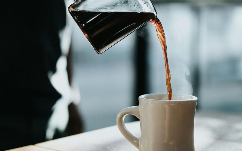 a person pouring a carafe of coffee into a cup