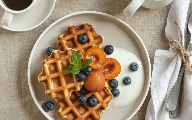 a plate of blueberries and waffles and a cup of coffee