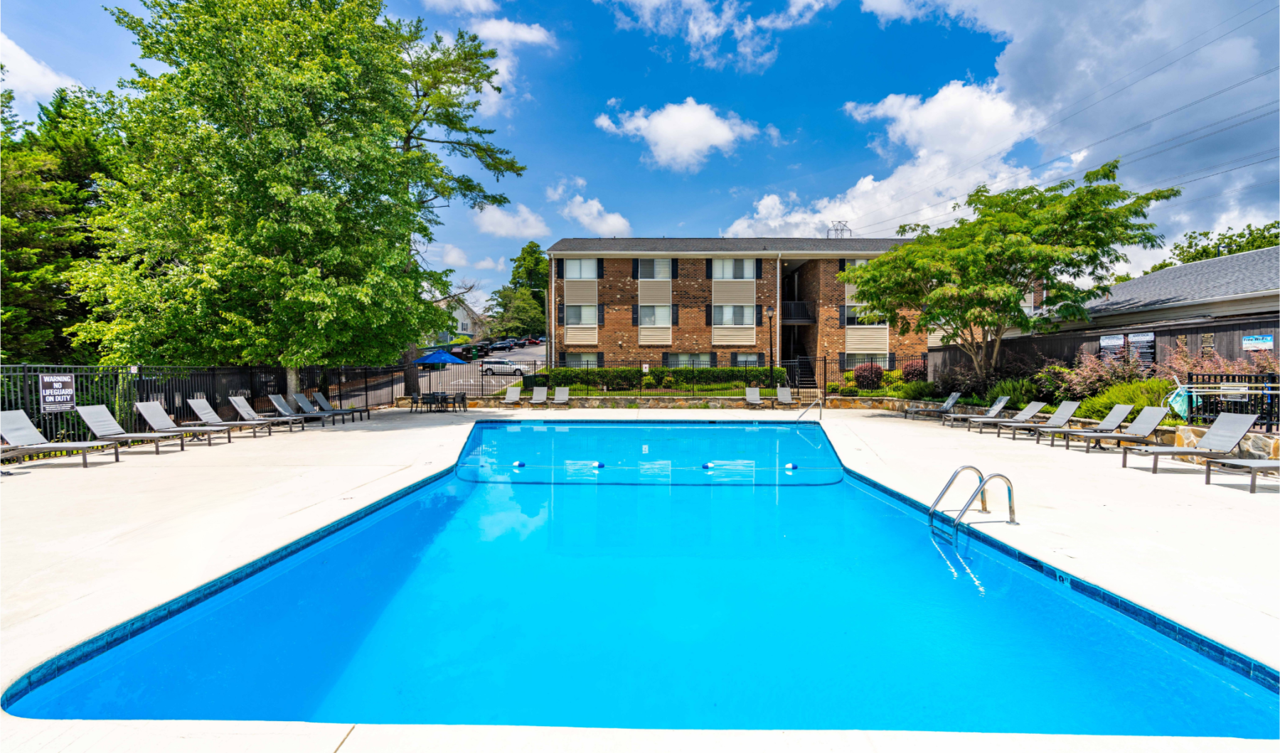 a swimming pool with a deck and chairs and trees in the background