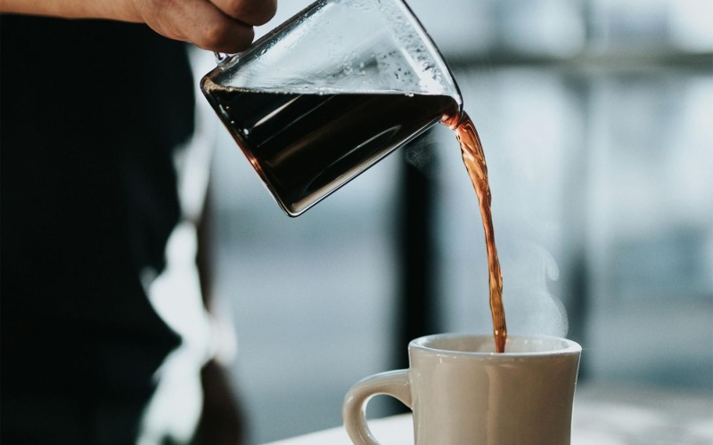 a person pouring a carafe of coffee into a cup