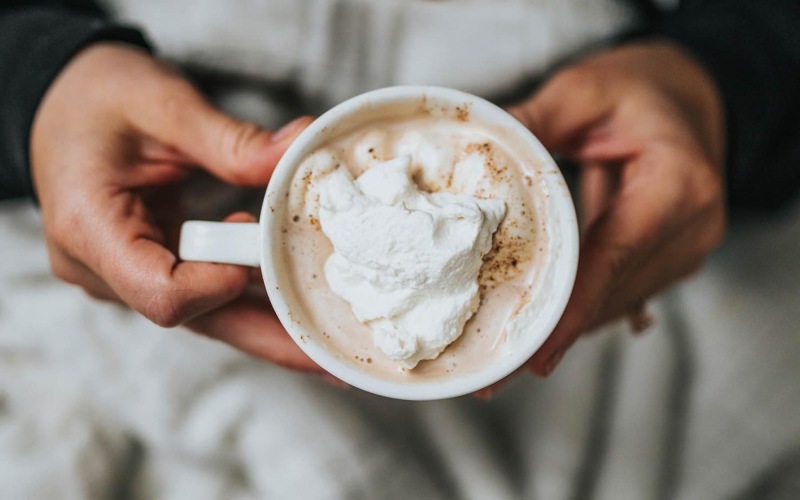 a person, in bed, holding a cup of coffee