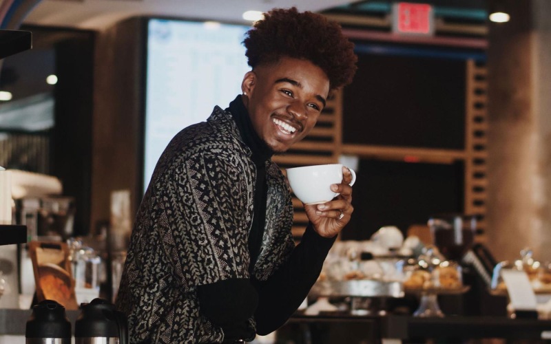 young man smiles while holding a cup of coffee in coffee shop