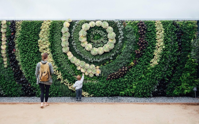 mother and child standing in front of a mural made of plants