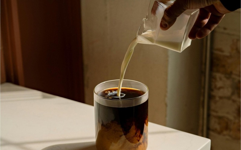 a hand pouring a cream into a coffee