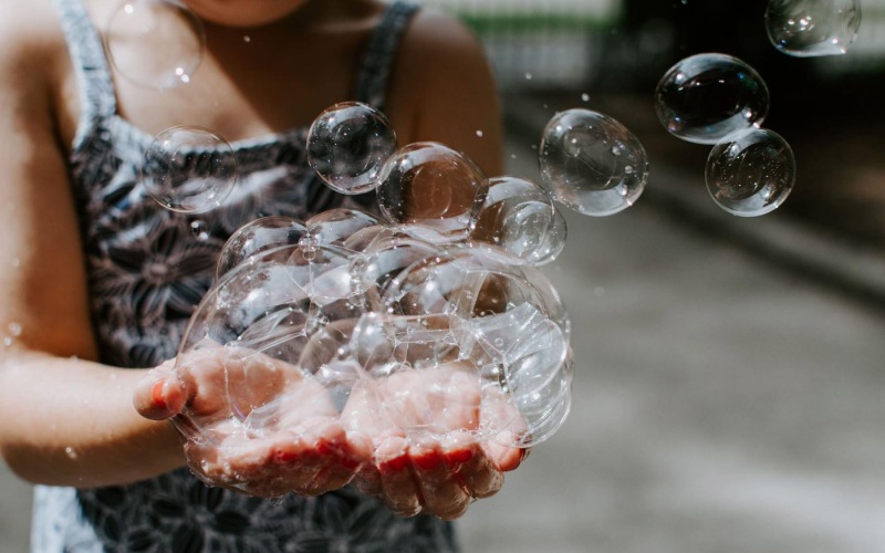 child holding bubbles in her hand as some float away