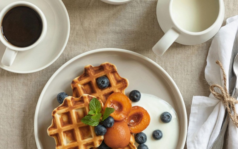 a plate of blueberries and waffles and a cup of coffee