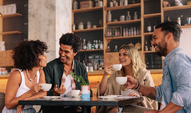 group of young adults smiling around a table over coffee in an urban cafe