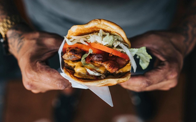 man holds a thick, juicy burger with both hands