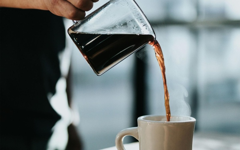 a person pouring a carafe of coffee into a cup