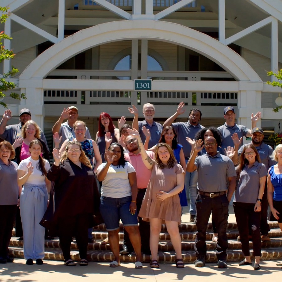 A group of GSC employees stand outside waving at the camera