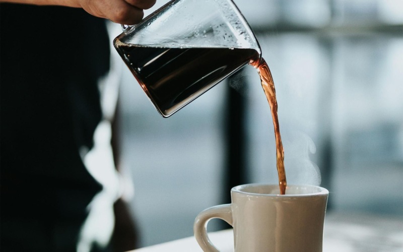 a person pouring a carafe of coffee into a cup