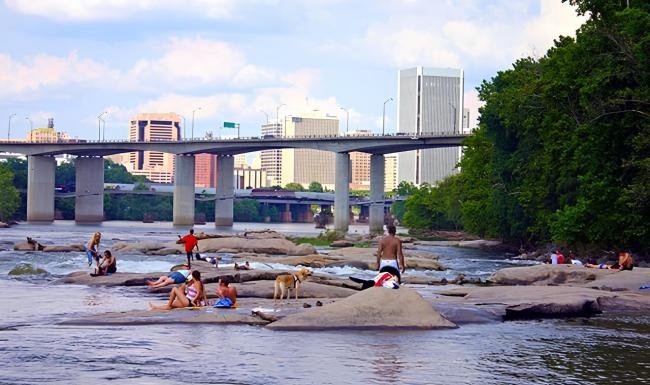people sitting on rocks in the water with a bridge in the background