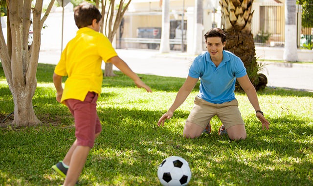 father and son playing soccer in a park