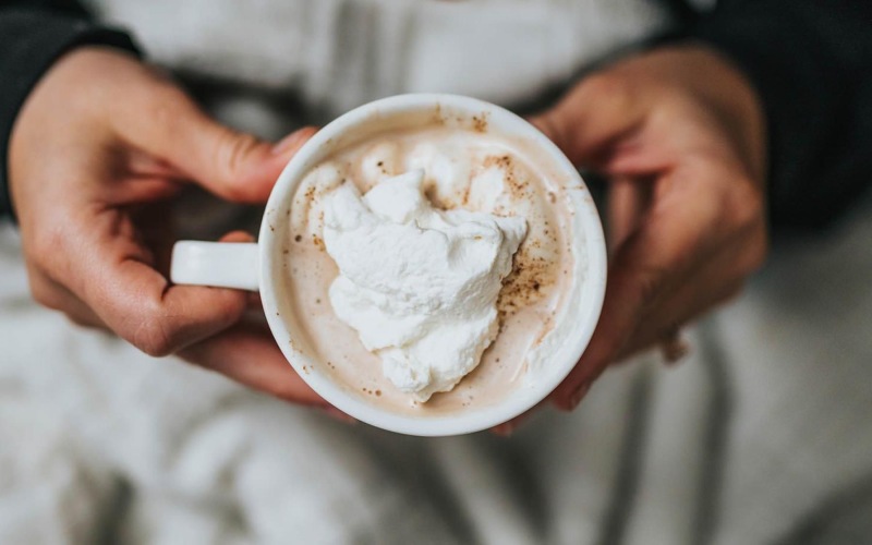 a person, in bed, holding a cup of coffee
