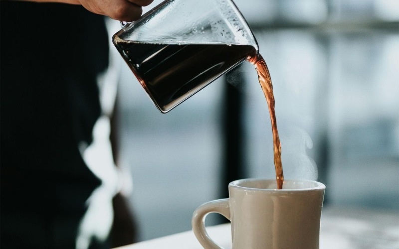 a person pouring a carafe of coffee into a cup