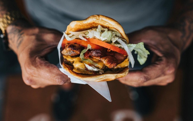 man holds a thick, juicy burger with both hands