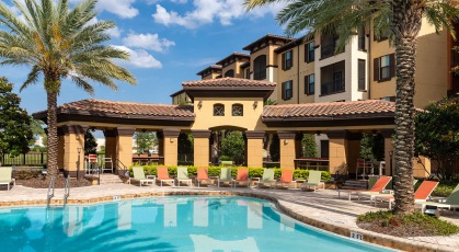 Landscaped pool area with palm trees, hedges and lounge chairs and tables