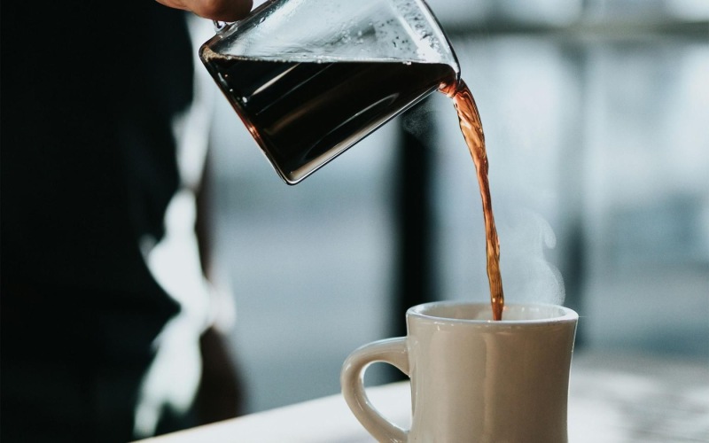 a person pouring a carafe of coffee into a cup