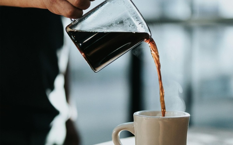 a person pouring a carafe of coffee into a cup